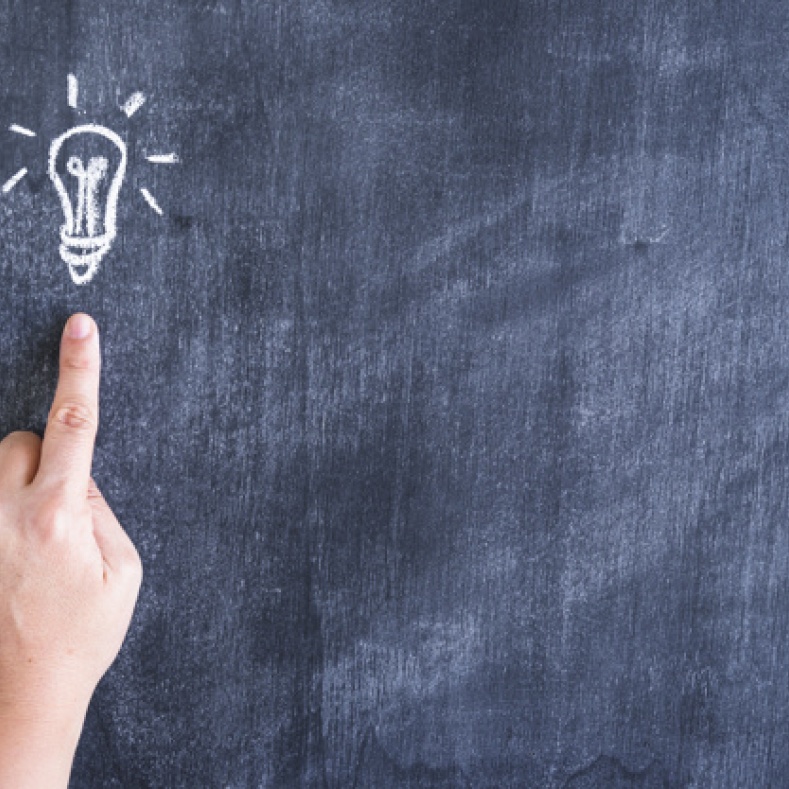 Finger points to a painted light bulb on a blackboard