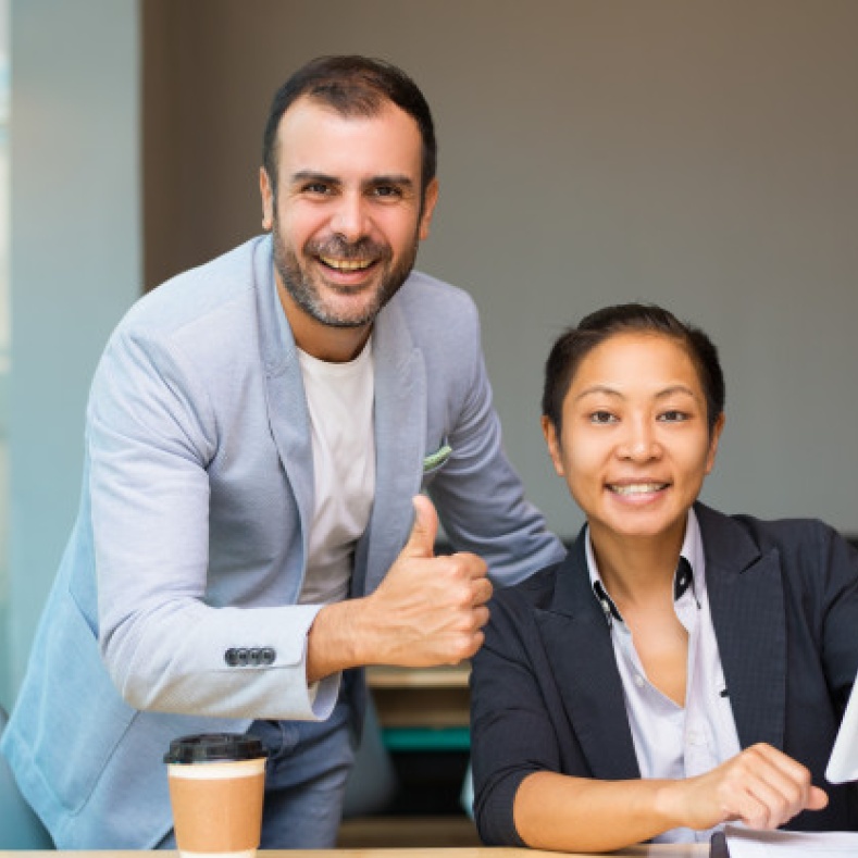 Two colleagues laugh into the camera at their workplace.
